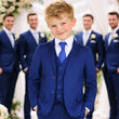 Young boy in a blue suit standing in front of a group of men in similar suits with floral decorations.