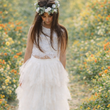 Woman in a white dress with a floral crown standing in a field of flowers.