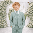 Young boy in a light blue suit standing in front of floral decorations