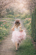 Young girl in a pink dress walking through a garden with cherry blossom trees.
