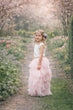 Young girl in a white top and pink tulle skirt standing in a garden with cherry blossoms.