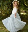 Young girl in a white lace top and light green tulle skirt with a floral crown outdoors.