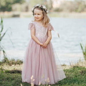 Young girl in a pink dress with a floral crown standing by a body of water.