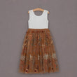 A sleeveless girl's dress hanging on a wooden hanger against a solid gray background. The dress features a white lace bodice and a tiered tulle skirt in a warm brown/bronze color with embroidered floral and leaf patterns.