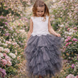 Young girl in a white top and gray tulle skirt standing in a flower garden.