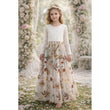 Young girl in a floral embroidered lace dress standing in a garden with flowers and chairs in the background