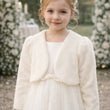 Young girl wearing a white dress with a matching shrug in a garden setting