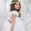 Young girl in a white dress with a floral headband against a textured white background