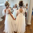 Two young girls in white dresses standing in front of a mirror.