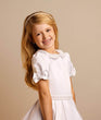Young girl wearing a white dress with a bow on a beige background