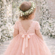 Child in a pink dress with a floral headband standing in front of a floral arch.