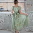 Young girl in a green floral dress standing against a textured wall.