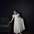 Young girl in a floral dress standing against a dark wall with a gray couch.