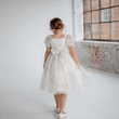 Young girl in a white lace dress standing in a room with brick walls.