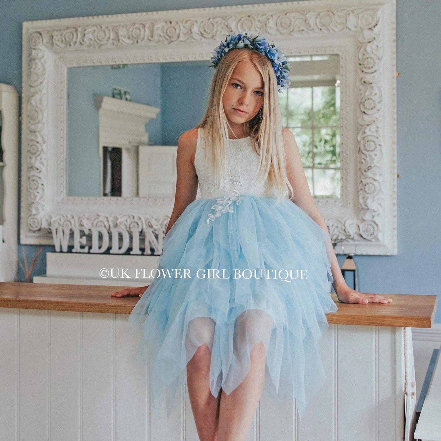 Girl in a white an blue party dress sitting in front of a mirror